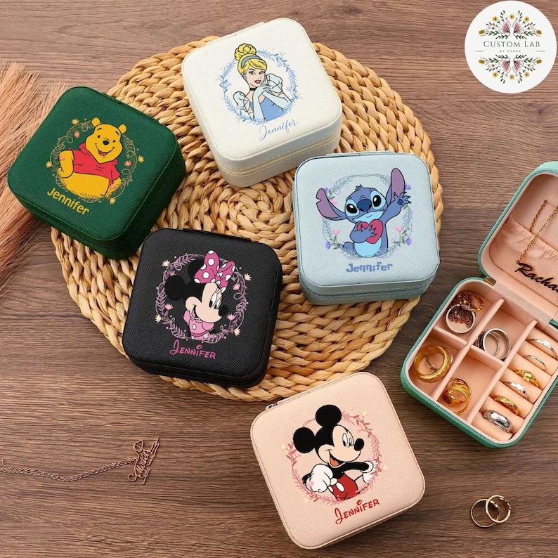 May include: A collection of square, zippered jewelry boxes featuring Disney characters like Winnie the Pooh, Cinderella, Minnie Mouse, Stitch, and Mickey Mouse. Each box has a character image and a name. One box is open, revealing rings and compartments.