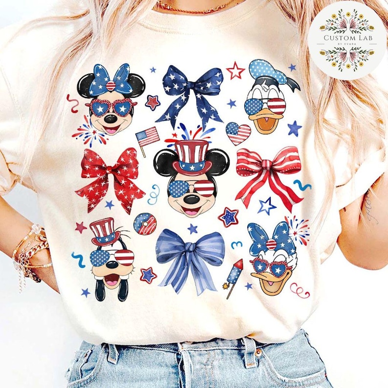 Peut inclure: Un t-shirt blanc &agrave; th&egrave;me patriotique rouge, blanc et bleu avec Mickey Mouse, Minnie Mouse, Donald Duck et Dingo portant des lunettes de soleil et des chapeaux rouge, blanc et bleu. Le t-shirt pr&eacute;sente &eacute;galement des n&oelig;uds et des &eacute;toiles rouge, blanc et bleu.
