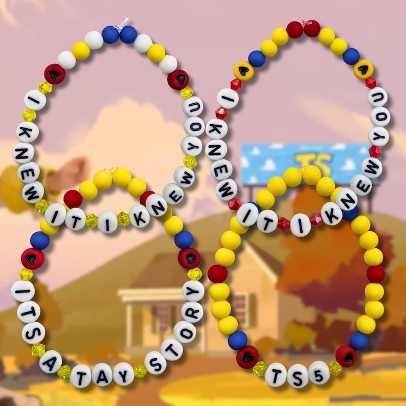 May include: Four circular beaded necklaces or bracelets featuring yellow, blue, red, and white beads. The white beads are printed with black letters spelling out the phrases I KNEW IT I KNEW IT and ITS A TAY STORY or TS5, interspersed with small yellow crystals.