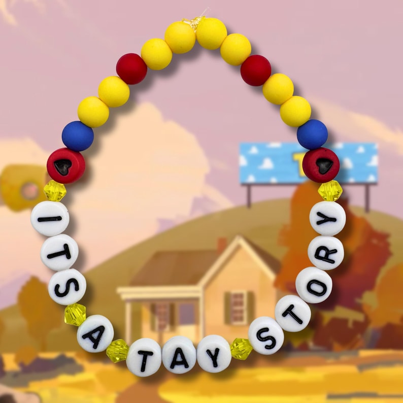 May include: A circular beaded bracelet featuring yellow, red, and blue spherical beads, interspersed with small yellow faceted beads. White round beads with black lettering spell out the phrase ITS A TAY STORY, with two red beads featuring black heart icons.