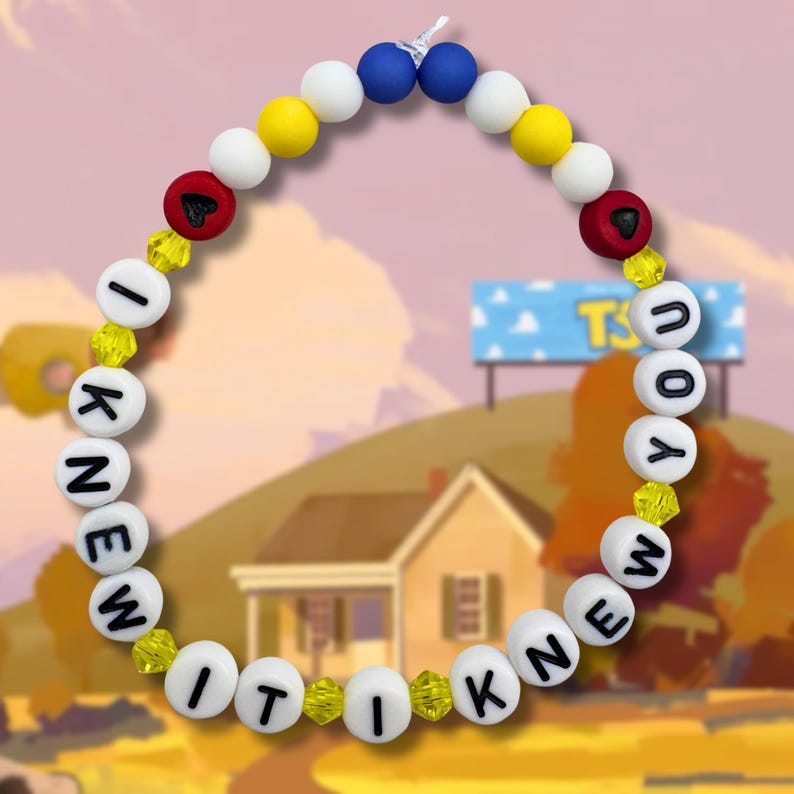 May include: A circular beaded bracelet featuring white spherical beads with black letters spelling out I KNEW IT I KNEW YOU. The design includes yellow, blue, and white round beads, two red beads with black heart symbols, and small yellow faceted beads.