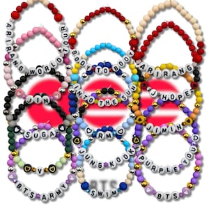 May include: A selection of colourful beaded bracelets. Each bracelet has a different colour scheme and includes white letter beads spelling out words and names such as "BTS ARMY", "JUNGKOOK", and "PURPLE YOU".