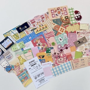 May include: A collection of colorful stickers, paper ephemera, and small cards with various designs. Includes a donut box, a Goldilocks book, a Target receipt, and a cartoon cat sticker. The items are arranged on a white surface.