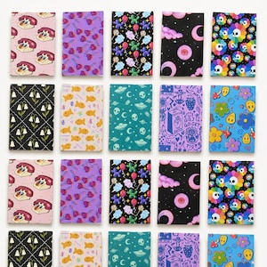 May include: A collection of twenty rectangular notebooks arranged in a grid, featuring diverse patterns including retro telephones, purple lollipops, balloon animals, celestial moons, colorful skulls, white flowers, goldfish, aliens, and smiley faces.