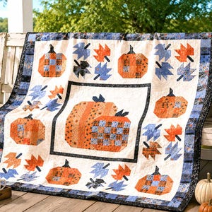 May include: A rectangular quilt featuring a central block with two large pumpkins surrounded by smaller pumpkin and leaf motifs. The design uses a color palette of orange, blue, and black on a cream background with a dark patterned border.