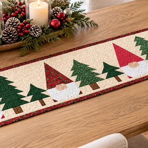 May include: A rectangular quilted table runner featuring a repeating pattern of gnomes with red and patterned hats, white beards, and green pine trees on a cream background, finished with a red and green patterned border trim.