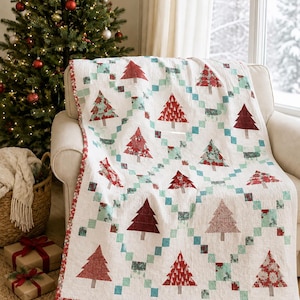 May include: A white quilt featuring a repeating pattern of Christmas trees in various shades of red and green, arranged within a lattice of small teal and green squares. The quilt has a red patterned border and is draped over a light-coloured chair.