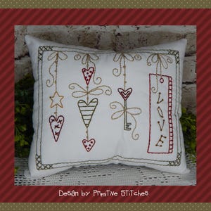 Könnte beinhalten: Ein weißes Kissen mit gestickten Herzen, Sternen, Schlüsseln und dem Wort "LOVE" in rotem Faden. Das Kissen ist im rustikalen Vintage-Stil verziert.