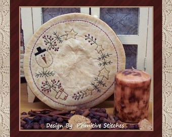 May include: A beige round fabric with a snowman, stars, and sprigs of greenery embroidered in green and red thread. The fabric is on a wooden surface with a brown candle and cinnamon sticks.