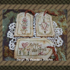 May include: Three handmade fabric tags with embroidery. The tags are cream colored with red, green, and brown embroidery. The tags feature hearts, flowers, and the text "Happy Valentines".