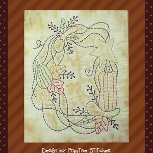 May include: A vintage-style embroidery design featuring a star, pumpkins, and leaves in shades of brown, green, and red. The design is stitched on a cream-colored fabric and includes the text "Design by Primitive Stitches".