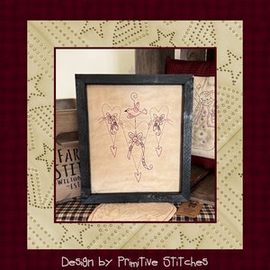 Peut inclure: Tableau encadr&eacute; avec un motif d'oiseau et de c&oelig;urs, cousu en fil rouge sur un fond beige. L'&oelig;uvre est dans un cadre noir. Les mots "Design by Primitive Stitches" sont en bas de l'image. L'&oelig;uvre est expos&eacute;e sur une surface &agrave; carreaux.