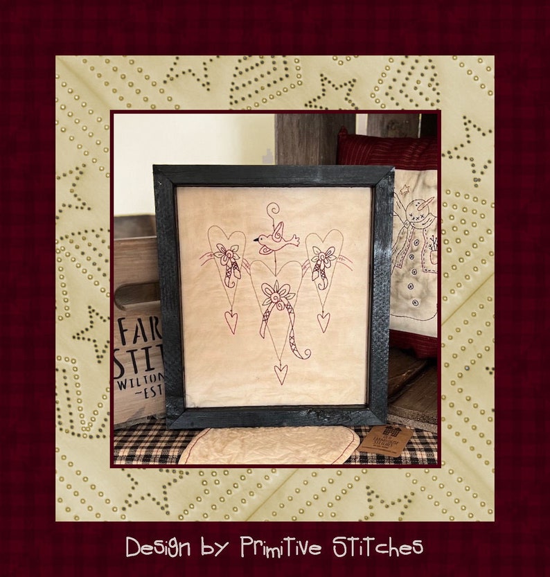 Peut inclure: Tableau encadr&eacute; avec un motif d'oiseau et de c&oelig;urs, cousu en fil rouge sur un fond beige. L'&oelig;uvre est dans un cadre noir. Les mots "Design by Primitive Stitches" sont en bas de l'image. L'&oelig;uvre est expos&eacute;e sur une surface &agrave; carreaux.