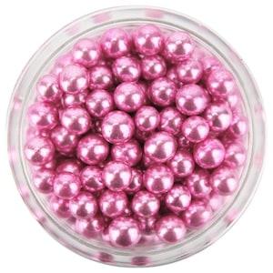 Puede incluir: Un tarro de cristal transparente lleno de numerosas bolas de caramelo rosa perlado. Las bolas de caramelo tienen una superficie brillante y reflectante y están densamente empaquetadas dentro del tarro. El tarro está sobre un fondo blanco.