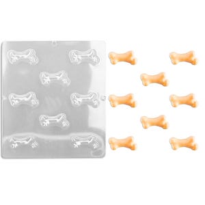 May include: A clear plastic mold with nine bone-shaped cavities.  Next to the mold are nine bone-shaped candies in a light orange color.
