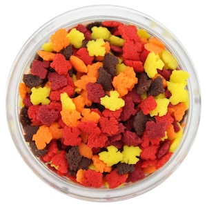 May include: A clear glass bowl filled with colourful leaf-shaped sprinkles. The sprinkles are in shades of red, orange, yellow, and brown. These decorative sprinkles are perfect for adding a festive touch to baked goods and desserts.
