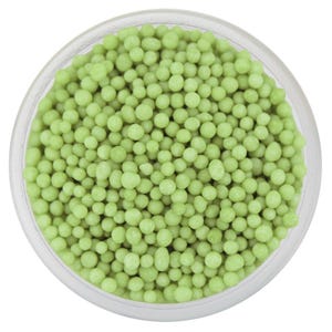 Puede incluir: Un recipiente de vidrio transparente lleno de pequeñas chispas redondas de color verde claro. Las chispas están densamente empaquetadas, creando una superficie texturizada. El recipiente está sobre un fondo blanco, resaltando el color vibrante de las chispas.