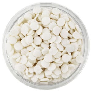May include: A clear glass jar filled with white, round sprinkles. The sprinkles are small, flat discs, and fill the jar to the top. The jar is sitting on a white surface. The sprinkles appear to be for baking or decorating.