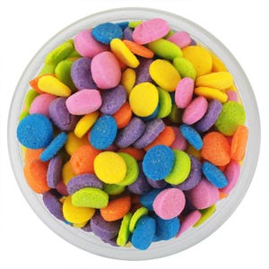 May include: A clear glass bowl filled with a collection of small, round, flat, multi-colored sugar candies. The candies are vibrant shades of pink, purple, blue, yellow, orange, and lime green, creating a dense, textured, and colorful display.