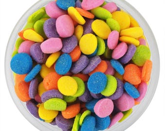 May include: A clear glass bowl filled with a collection of small, round, flat, multi-colored sugar candies. The candies are vibrant shades of pink, purple, blue, yellow, orange, and lime green, creating a dense, textured, and colorful display.