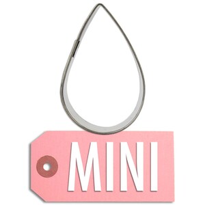 May include: A silver metal cookie cutter shaped like a teardrop. The cookie cutter is sitting on top of a pink tag with the word "MINI" printed in white.