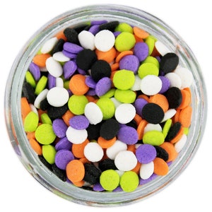 Op de afbeelding: Een heldere glazen pot gevuld met kleurrijke hagelslag. De hagelslag is in verschillende vormen en kleuren, waaronder wit, zwart, oranje, paars en groen. De hagelslag is klein en rond en is verspreid door de pot. De pot staat op een witte ondergrond.