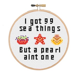Peut inclure: Un cerceau de broderie blanc avec le texte "I got 99 sea things but a pearl ain't one" et des images pixélisées d'une étoile de mer, d'un coquillage et d'une anémone de mer.