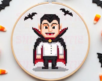 May include: A cross-stitch design of a vampire, framed in a wooden embroidery hoop. The vampire is depicted in pixel art style, wearing a black cape with a red interior, a white shirt, and black trousers. Halloween-themed decorations surround the hoop.