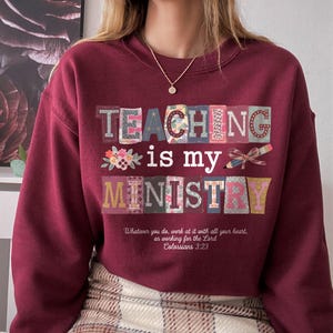 May include: A maroon long-sleeve sweatshirt featuring the text "TEACHING is my MINISTRY" in colorful, patterned block letters. Below the text, the phrase "Whatever you do, work at it with all your heart, as working for the Lord Colossians 3:23" is printed.