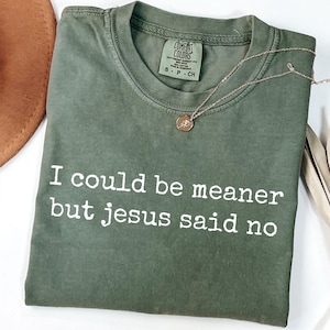 Pu&ograve; includere: Una t-shirt a maniche corte color verde oliva con la scritta bianca "I could be meaner but jesus said no" stampata sul davanti. La maglia presenta un girocollo e un'etichetta del marchio Comfort Colors all'interno del colletto che indica la taglia S.