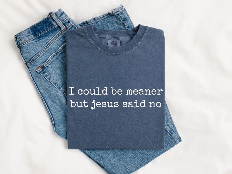 Pu&ograve; includere: Una t-shirt girocollo color blu ardesia con la scritta bianca "I could be meaner but jesus said no" stampata sul davanti, abbinata a un paio di jeans blu. La maglietta ha maniche corte e una vestibilit&agrave; standard.