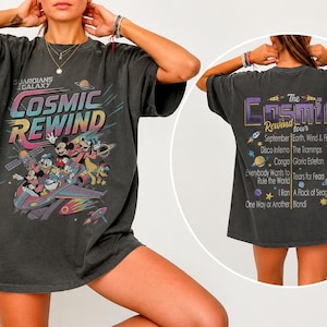 May include: A charcoal gray oversized t-shirt featuring a Guardians of the Galaxy Cosmic Rewind graphic on the front with Disney characters in a spaceship. The back displays The Cosmic Rewind tour text with a list of songs and artists.