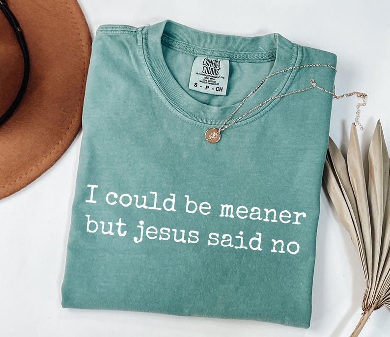 Pu&ograve; includere: Una t-shirt a maniche corte color verde salvia con scollo rotondo e la scritta bianca "I could be meaner but jesus said no" stampata sul davanti. La maglietta presenta un'etichetta del marchio Comfort Colors all'interno del collo ed &egrave; taglia S.