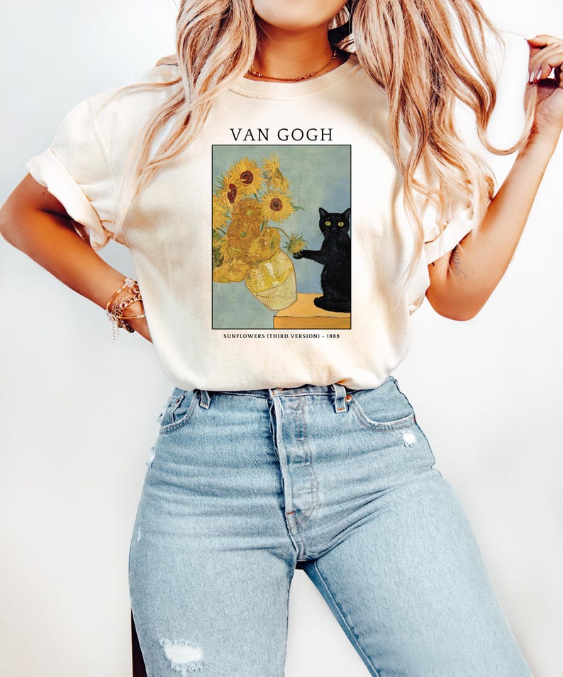 May include: Cream-colored t-shirt featuring a print of Van Gogh's "Sunflowers (Third Version)" with a black cat. The artwork includes a vase of sunflowers and the text "VAN GOGH" and "SUNFLOWERS (THIRD VERSION) - 1888".