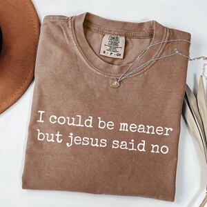 Pu&ograve; includere: Una t-shirt marrone a maniche corte con scollo rotondo e il testo bianco I could be meaner but jesus said no stampato sul davanti. La maglietta presenta un'etichetta del marchio Comfort Colors sul collo interno con la taglia S-P-CH indicata.
