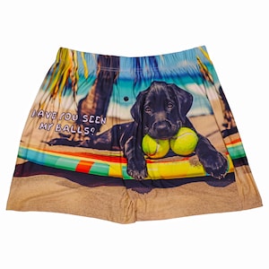 May include: A pair of men's boxer shorts with a black Labrador puppy on a surfboard on a beach. The puppy is holding two tennis balls. The text "HAVE YOU SEEN MY BALLS?" is printed on the shorts.