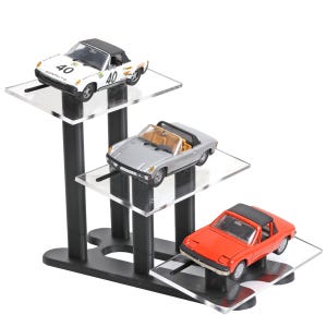 May include: A three-tiered display stand holding three toy convertible cars. The cars are white, silver, and red. The white car has the number 40 on it. The stand is black with clear acrylic shelves.