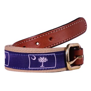 May include: A brown leather belt with a tan canvas strap featuring the South Carolina state flag. The flag is blue with a white crescent moon and palmetto tree.
