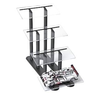 May include: A multi-tiered display stand with clear acrylic shelves and a black metal frame. A white and black race car model with red accents sits on the bottom shelf. The stand is designed to showcase collectibles.