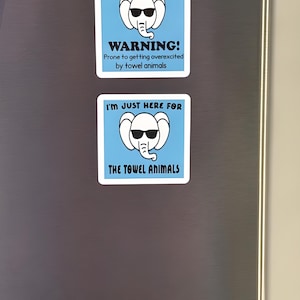 Op de afbeelding: Twee vierkante stickers met een blauwe achtergrond en witte rand. Elk heeft een cartoon-olifant met een zonnebril. De bovenste sticker luidt: "WARNING! Prone to getting overexcited by towel animals." De onderste sticker zegt: "I'M JUST HERE FOR THE TOWEL ANIMALS."