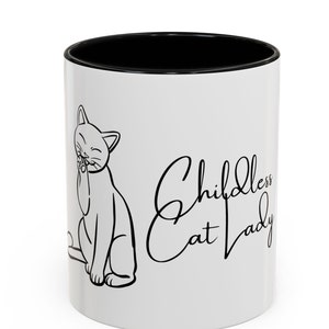 May include: White ceramic mug with a black rim. The mug features a black line drawing of a cat washing its face and the text "Childless Cat Lady" in a cursive font.