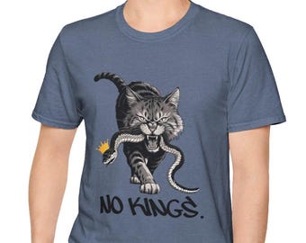 May include: A blue t-shirt featuring a graphic of a gray cat with a snake in its mouth, wearing a gold crown. The text "NO KINGS" is printed below the cat in a stylized font.