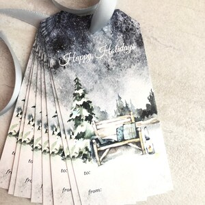 May include: A stack of gift tags with a winter scene watercolor design. The tags feature a snowy landscape with a bench, trees, and the words "Happy Holidays". Each tag has space to write "to" and "from". A silver ribbon is attached.