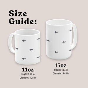 May include: Two white ceramic mugs with a shark pattern are displayed against a neutral background. The text "Size Guide:" is at the top. The 11oz mug is 3.74 inches high and 3.15 inches in diameter. The 15oz mug is 4.61 inches high and 3.43 inches in diameter.