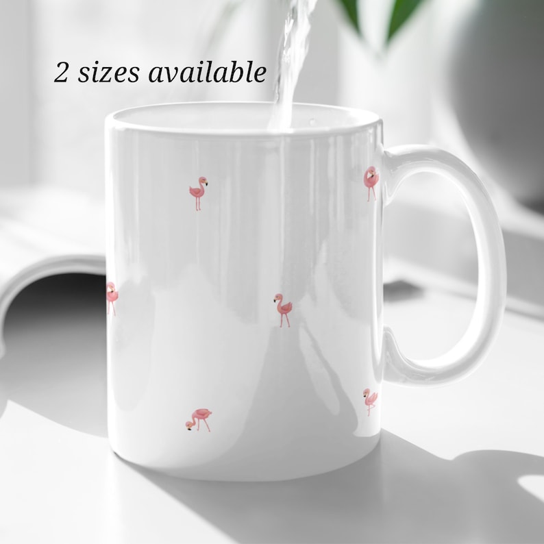 May include: White ceramic mug with a pink flamingo pattern. The mug has a handle and says "2 sizes available" on the front.