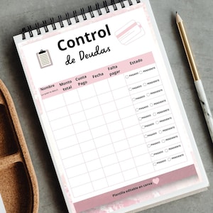 May include: A spiral-bound notepad with a debt control template in Spanish. The pink and white design includes fields for name, total amount, payment, and due date. A pencil rests beside the notepad.