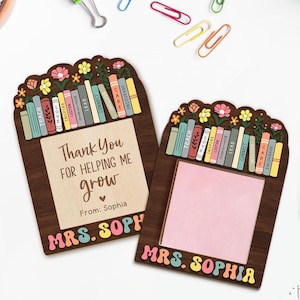 May include: Two wooden teacher appreciation gifts with a stack of books with words like 'teach', 'love', 'inspire', 'listen', 'lead', 'connect', 'care', and 'encourage'. The top gift has a thank you message that says 'Thank you for helping me grow' and 'From: Sophia'. The bottom gift has a blank space for writing a message and the name 'MRS. SOPHIA' on both gifts.