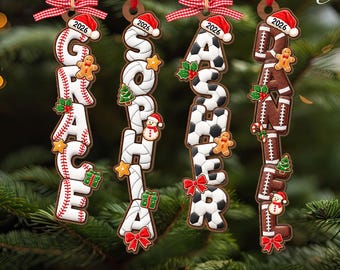 May include: Four vertical hanging ornaments featuring the names GRACE, SOPHIA, ASHER, and DANIEL. Each letter is shaped like a sports ball, including baseball, volleyball, soccer, and football textures, topped with a red Santa hat labeled 2026.
