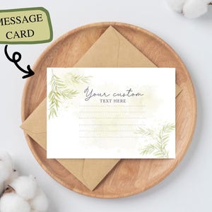 May include: A white message card with green watercolor leaves and the text "Your custom text here" sits on a wooden plate with a brown envelope. The card is labeled "MESSAGE CARD" in a green box.
