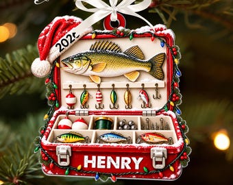 May include: A red tackle box Christmas ornament featuring a large fish, fishing lures, and hooks. The box is decorated with a Santa hat, Christmas lights, and the name HENRY. A white ribbon is attached to the top for hanging.